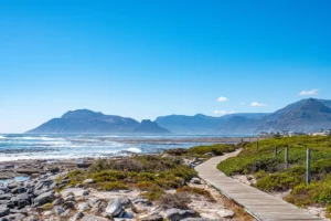 Südafrikas Strand mit Felsen, Bergen, Felsstrand und Meer. Ein Holzweg führt am Strand entlang.